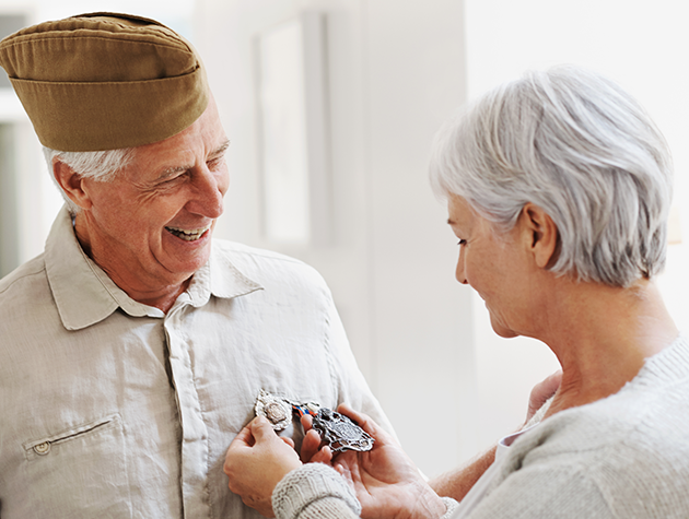 Elderly woman pinning a medal on the shirt of an elderly veteran man.